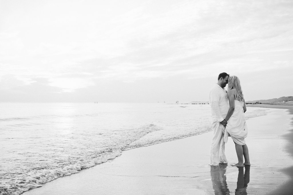 Photo black & white picture of bride and groom kissing while standing in wet sand